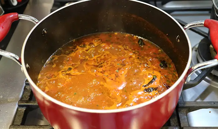 The Bombay potato curry recipe (Bombay Bataka) cooking in a red saucepan over the hob. 